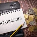 Notebook with Stablecoin written and various coins on desk